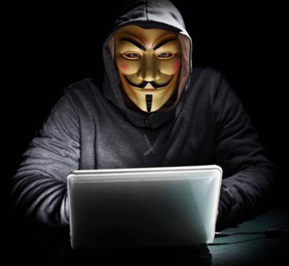 Hacker in a hoodie with an annonymous mask using a laptop